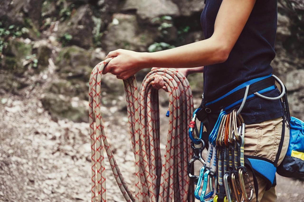 Climber woman wearing in safety harness with equipment holding rope and preparing to climb